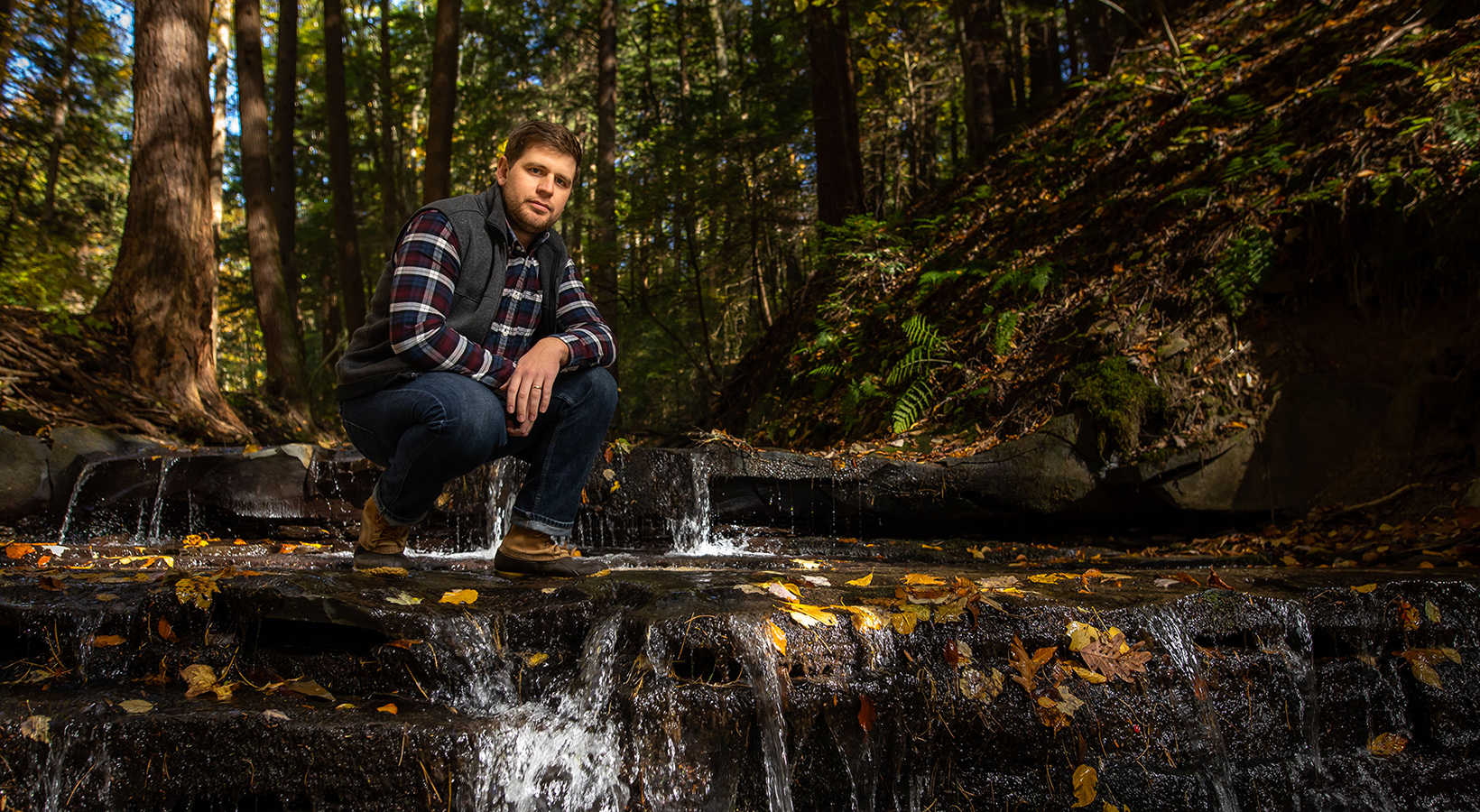 Joshua Lewis kneeling beside creek
